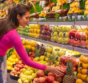 A woman in a bright pink top selecting fresh fruits in a Hypermarket produce aisle.